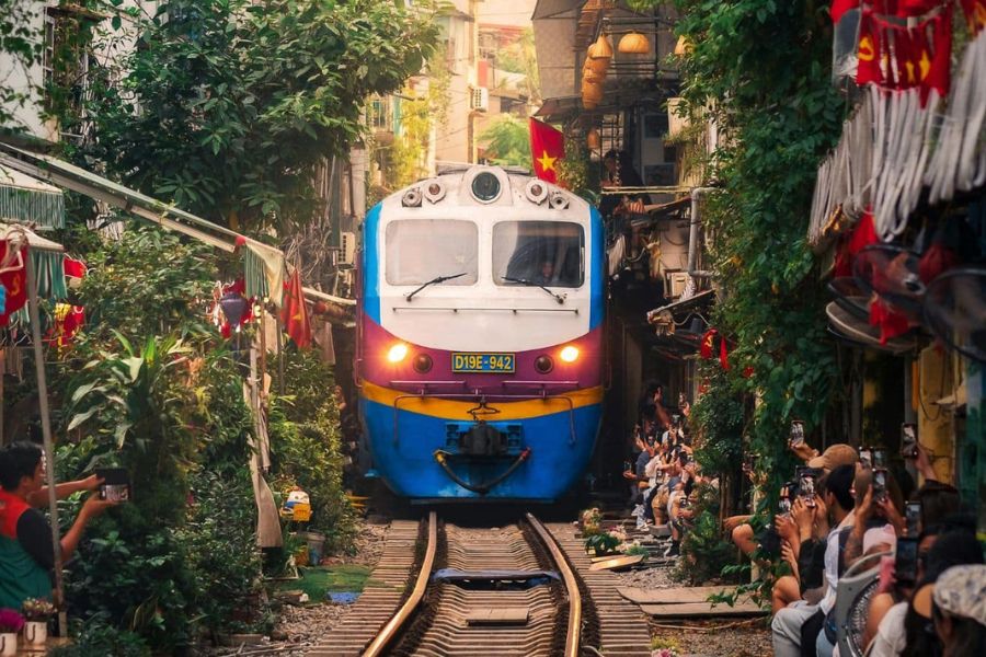 Artistic slow-shutter motion blur photograph of the Reunification Express train rushing through warmly lit lantern cafes along Hanoi Train Street