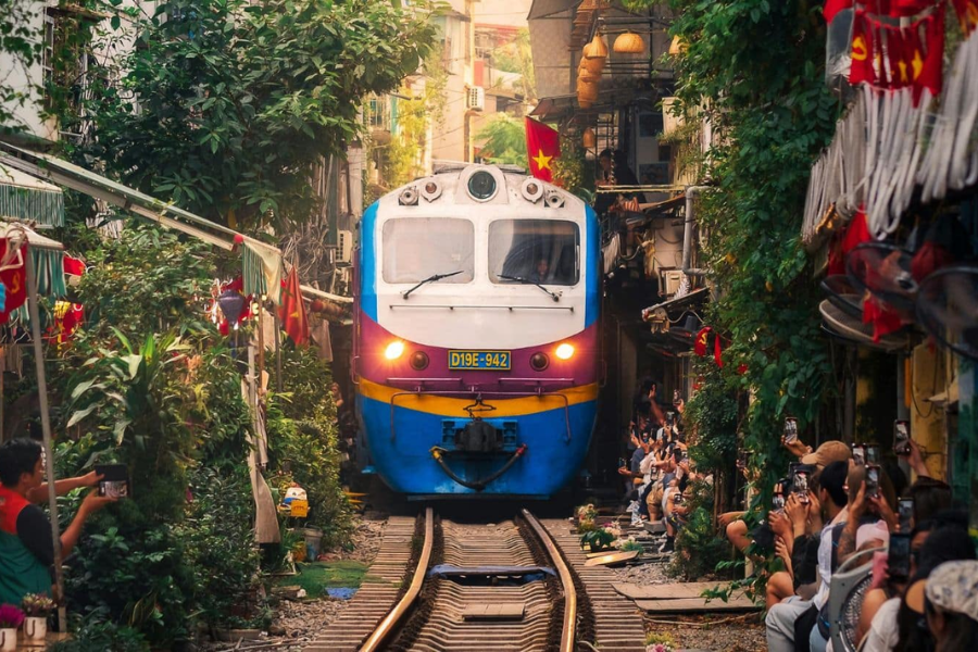 Artistic slow-shutter motion blur photograph of the Reunification Express train rushing through warmly lit lantern cafes along Hanoi Train Street