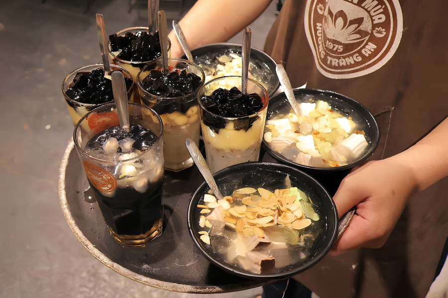 Refreshing bowl of chilled sweet soup with tender lotus seeds, longan fruit, and jasmine blossom syrup served in a classic Hanoi dessert shop
