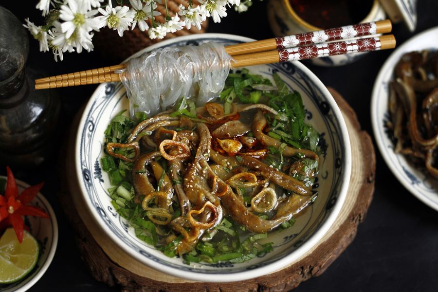 Tossed glass noodle bowl with crispy fried swamp eel, fresh Vietnamese coriander, cucumber, roasted peanuts, and fried shallots in a Hanoi heritage stall