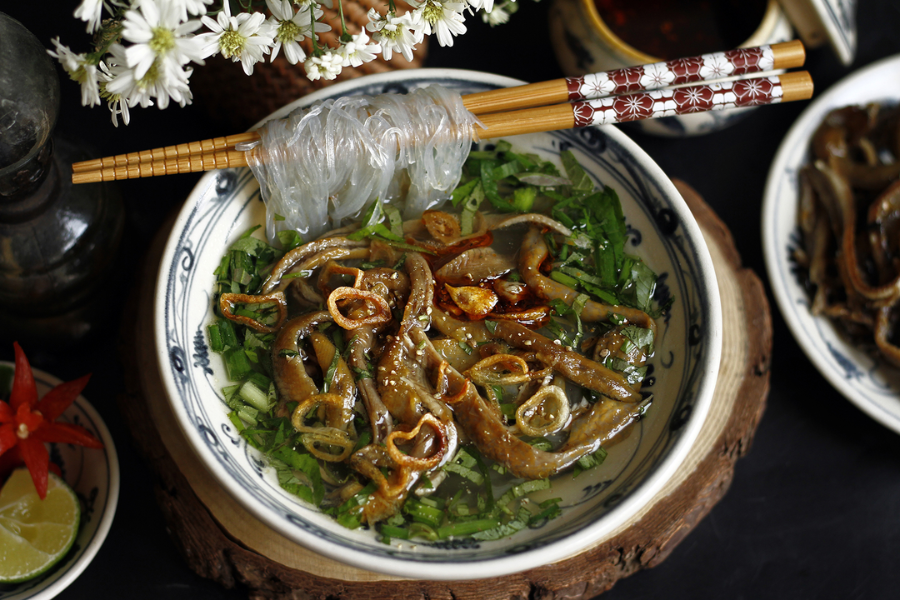 Tossed glass noodle bowl with crispy fried swamp eel, fresh Vietnamese coriander, cucumber, roasted peanuts, and fried shallots in a Hanoi heritage stall