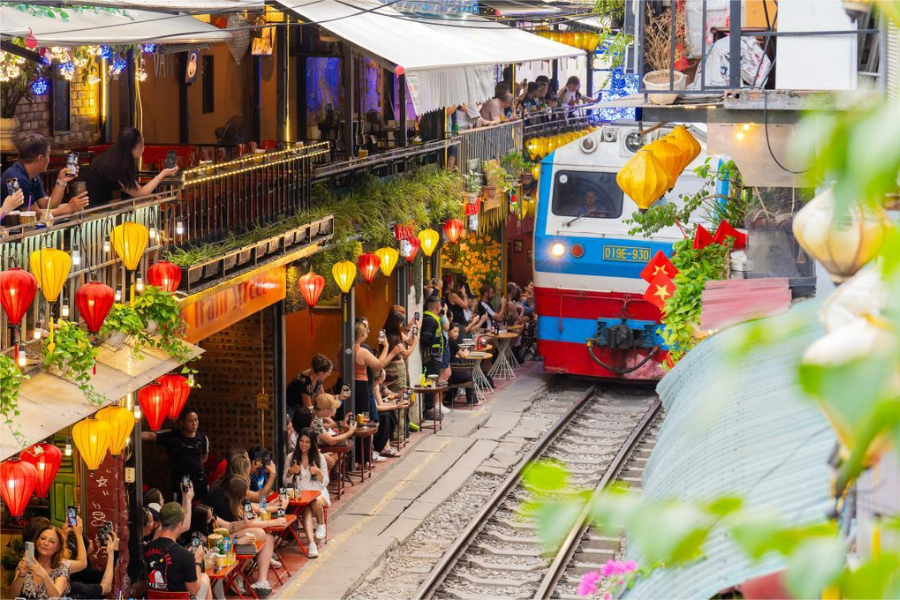 Elevated perspective from a private wooden second-story cafe balcony overlooking the narrow railway tracks and passing train on Hanoi Train Street