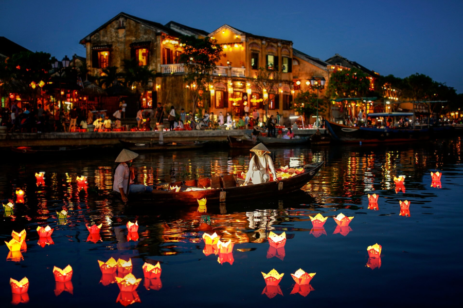 Close-up of hands releasing a glowing flower paper candle lantern onto calm river waters