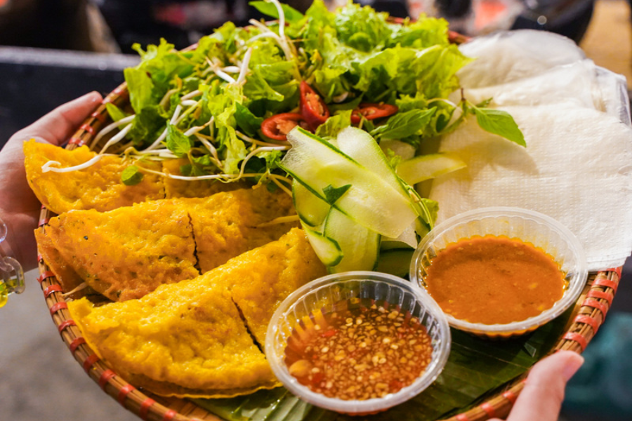 Golden crispy Vietnamese turmeric pancake stuffed with freshwater shrimp, pork, and fresh bean sprouts, served alongside fresh herbs and rice paper wrappers