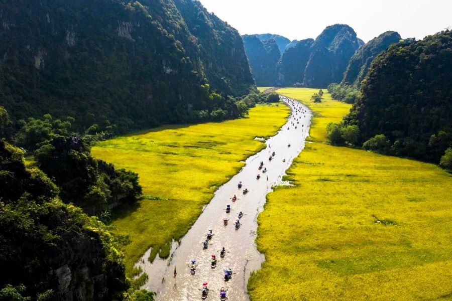 Traditional wooden sampan boat floating along the tranquil Ngo Dong River past limestone peaks in Ninh Binh