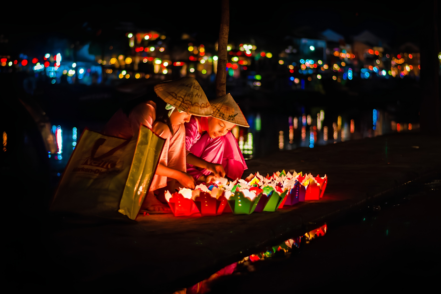 A wooden boat passenger releasing floating candle lanterns onto the Hoai River in Hoi An ancient town.
