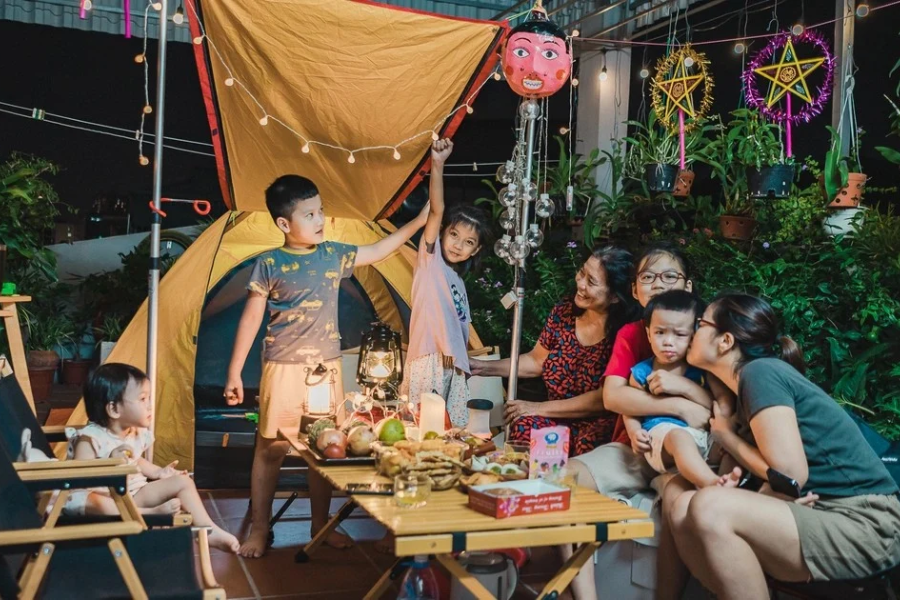 A multi-generational family gathering happily around a decorated full moon fruit and pastry feast table