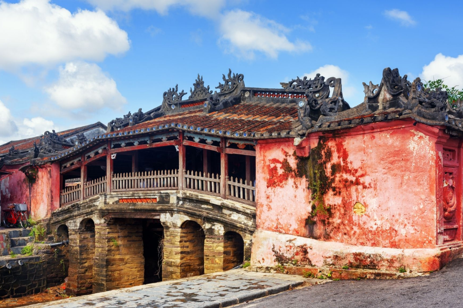 Historic curved Japanese Covered Bridge with timber railings and tiled roof over a canal in Hoi An