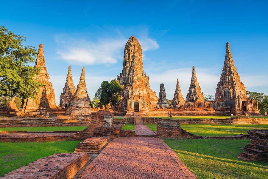 Ancient bell-shaped stone chedis and brick ruins under a bright blue sky at Ayutthaya Historical Park
