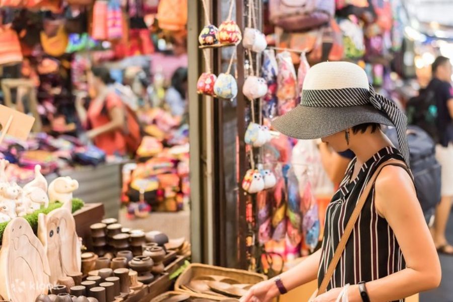 Artisan vendor arranging handmade celadon ceramics and wooden craft decor in an open-air stall at Chatuchak Market