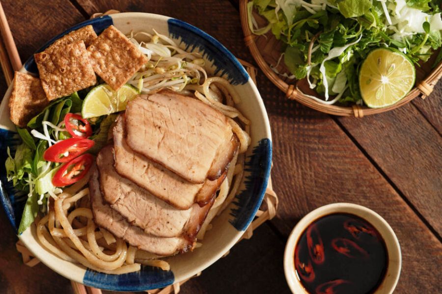 Bowl of authentic Cao Lau noodles topped with roasted pork slices, crispy crackling, and fresh herbs in Hoi An