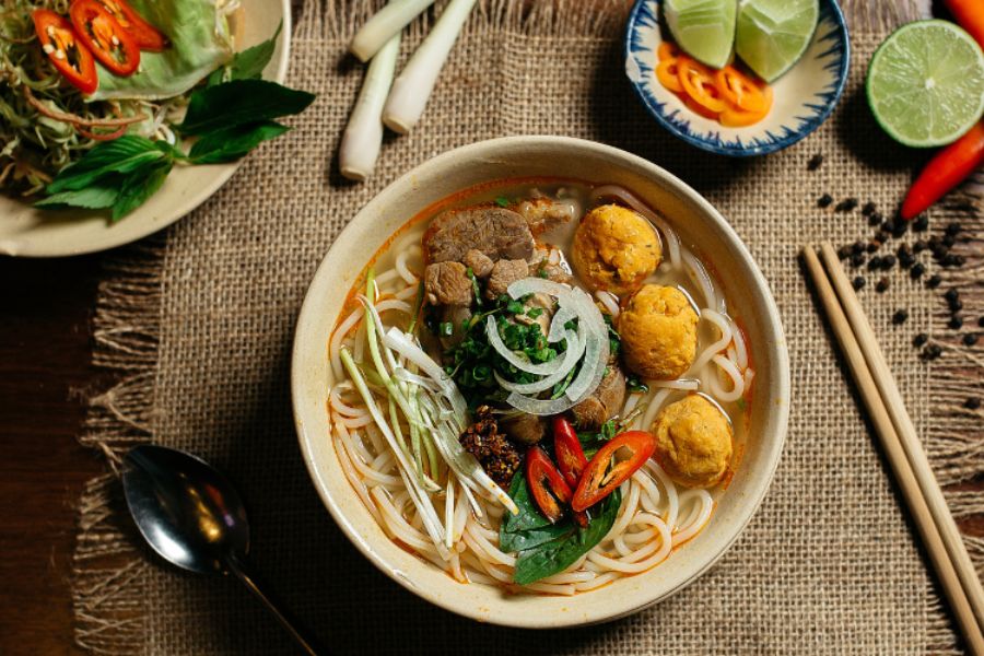 Bowl of bun bo Hue with beef, rice noodles, herbs and chilli in Hue