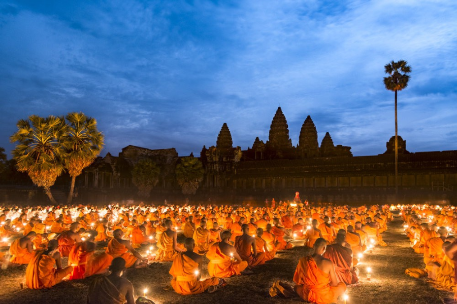 Hundreds of Buddhist monks and pilgrims carrying lit beeswax candles and lotus buds in a slow procession around a sacred stupa at night
