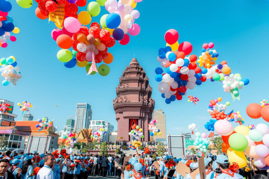 The red sandstone Independence Monument in Phnom Penh surrounded by fluttering national flags and blooming red flowers under a bright morning sky