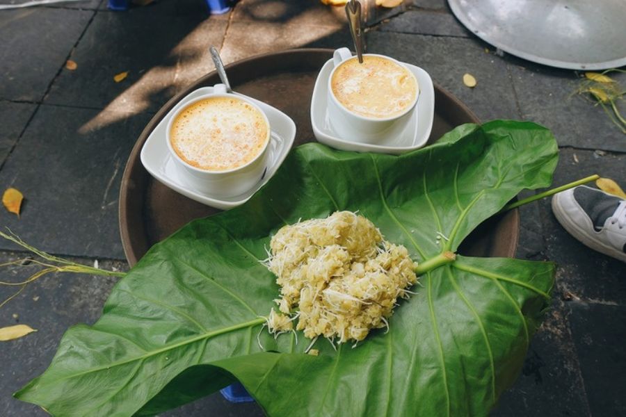 Fresh green young rice flakes com lang vong wrapped in vibrant lotus leaves tied with dried rice straw beside egg coffee