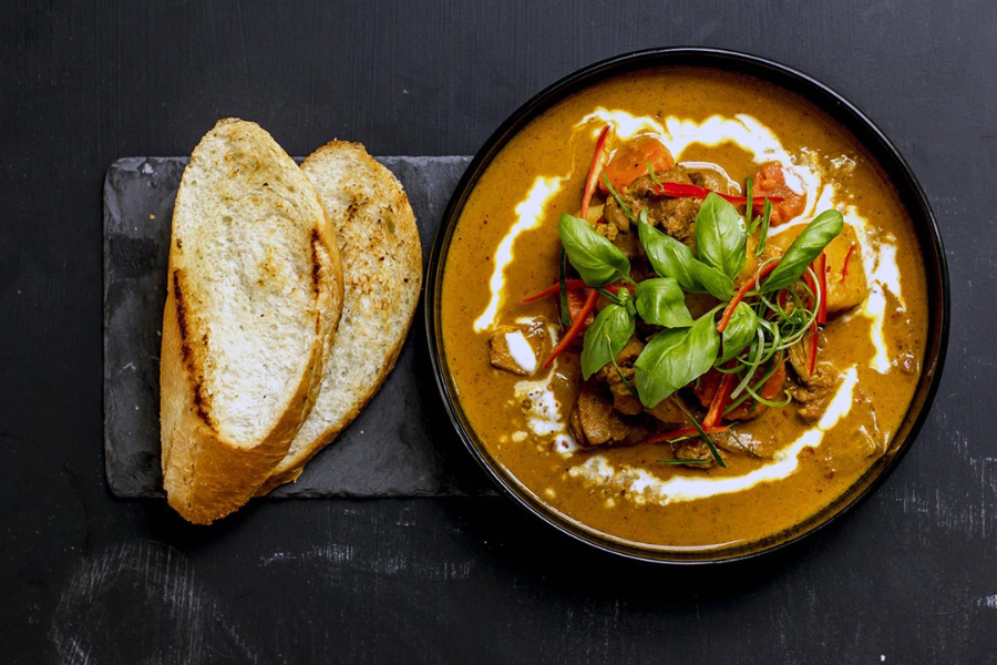A warm bowl of rich red coconut chicken curry with braised sweet potatoes served alongside a crusty French baguette