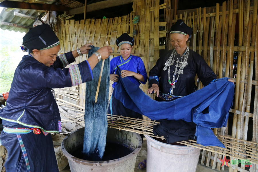 A H'Mong artisan using a traditional copper pen with hot beeswax to draw geometric batik patterns on dark indigo-dyed hemp cloth