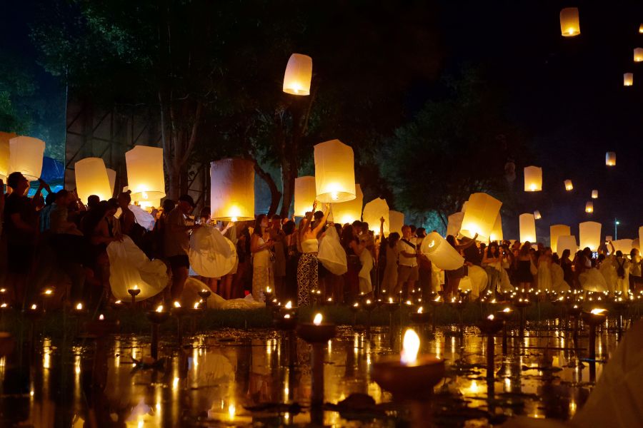 A family launching candlelit flower floats onto a calm garden lake before releasing sky lanterns in Doi Saket Chiang Mai