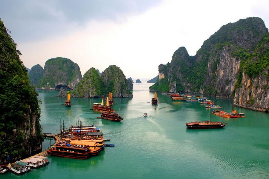 A luxury wooden boutique cruise ship sailing peacefully through calm waters between misty limestone karst towers in Halong Bay