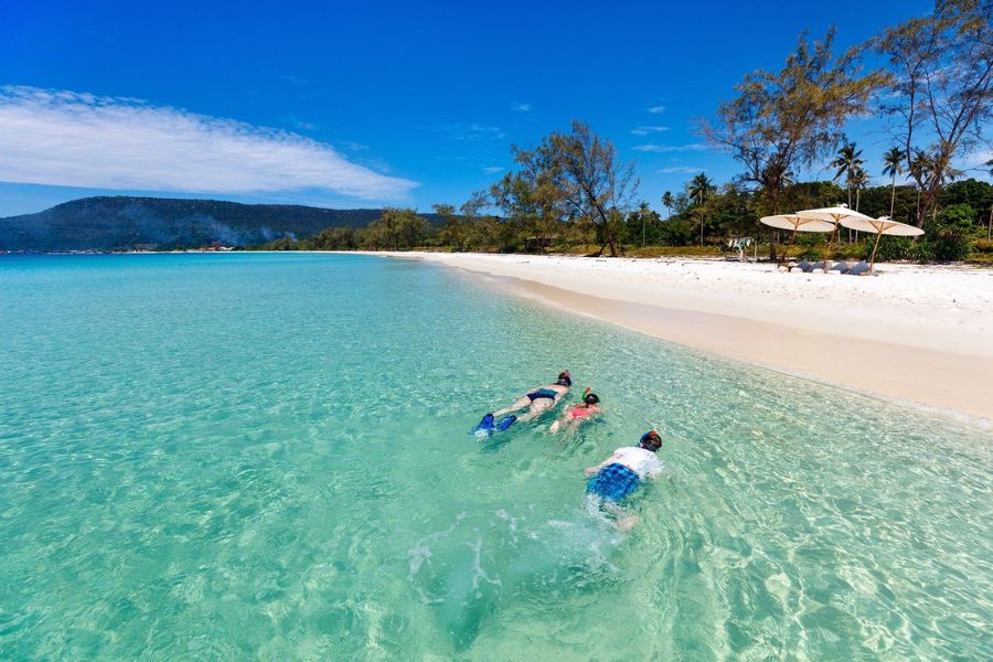 Crystal-clear turquoise water gently lapping onto soft white sand beaches lined with palm trees on Koh Rong Island in southern Cambodia