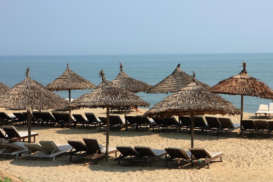 Thatched umbrella daybeds and golden sand facing gentle blue waves at An Bang Beach near Hoi An