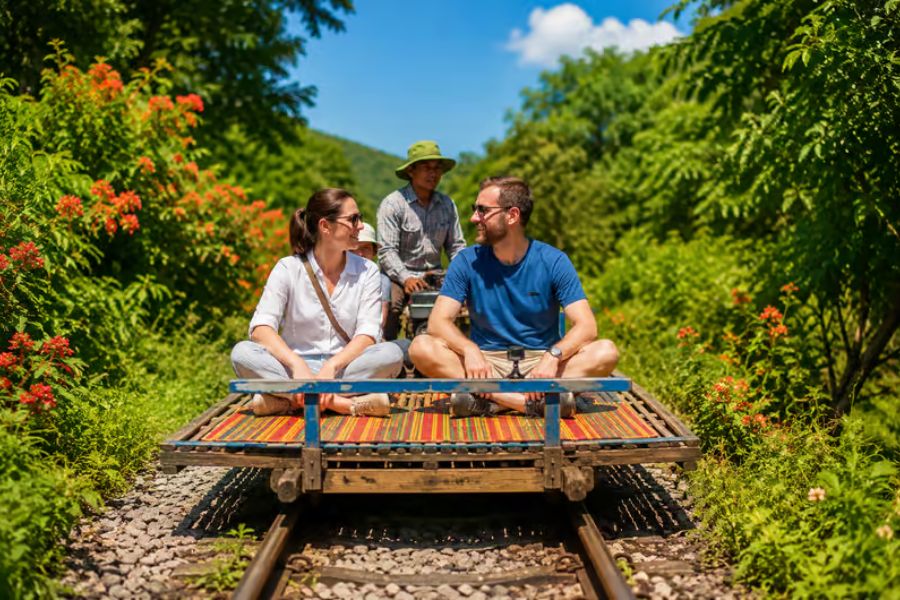 Traditional wooden and bamboo platform train running along old railway tracks through green open rice fields in Battambang