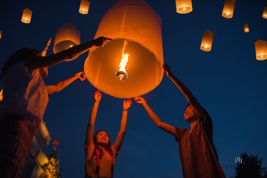 A devotee dressed in white holding a glowing rice paper Khom Loi lantern with hands together in prayer before releasing it into the sky