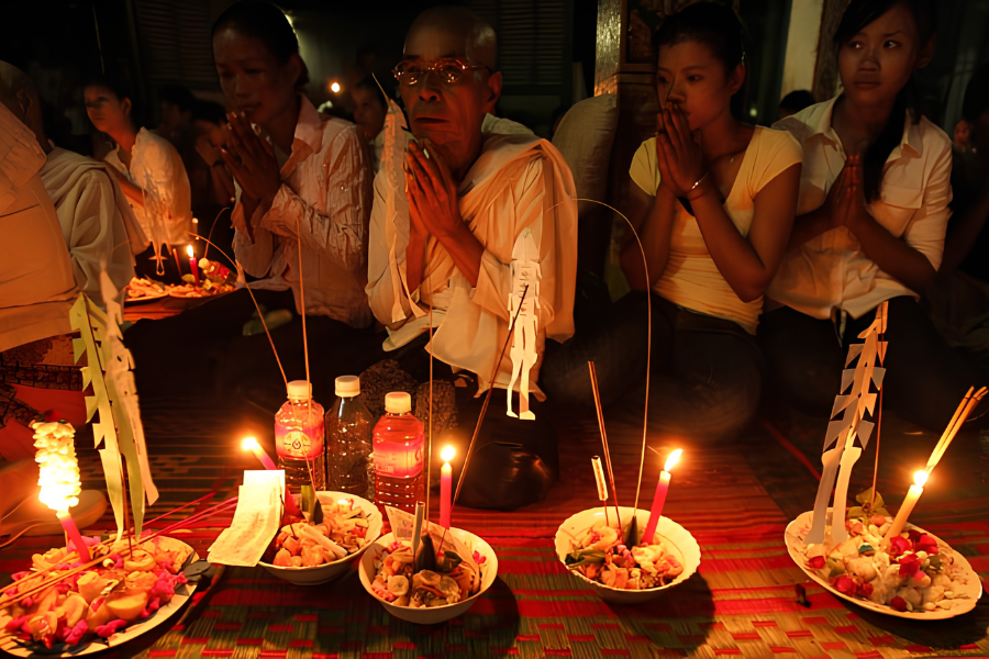 Cambodian devotees in white walking silently before dawn holding brass trays with sticky rice offerings during the Pchum Ben festival