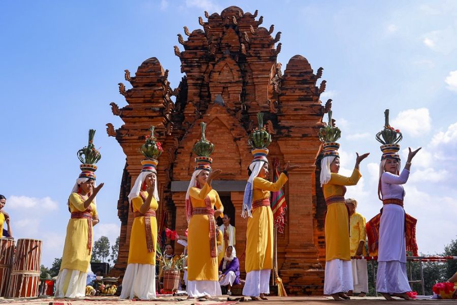 Cham women in traditional white and gold silk tunics performing graceful fan dances before the ancient Po Klong Garai Cham towers