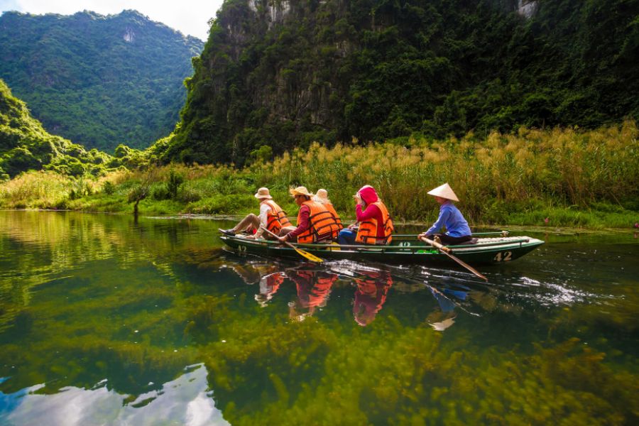 Wooden rowboat drifting along clear waterways between towering karst peaks and water lilies in Trang An, Ninh Binh