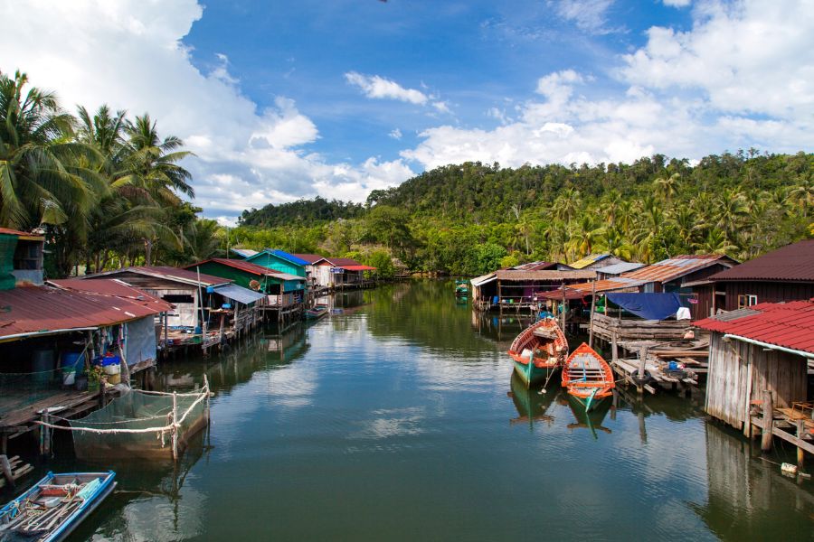 Traditional tall wooden stilted houses and small fishing boats along the riverbank in Kompong Phluk floating village on Tonle Sap Lake