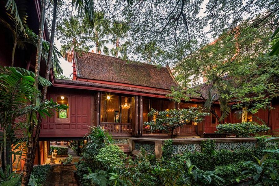 Traditional red teakwood houses surrounded by lush tropical gardens and ponds at Jim Thompson House in Bangkok