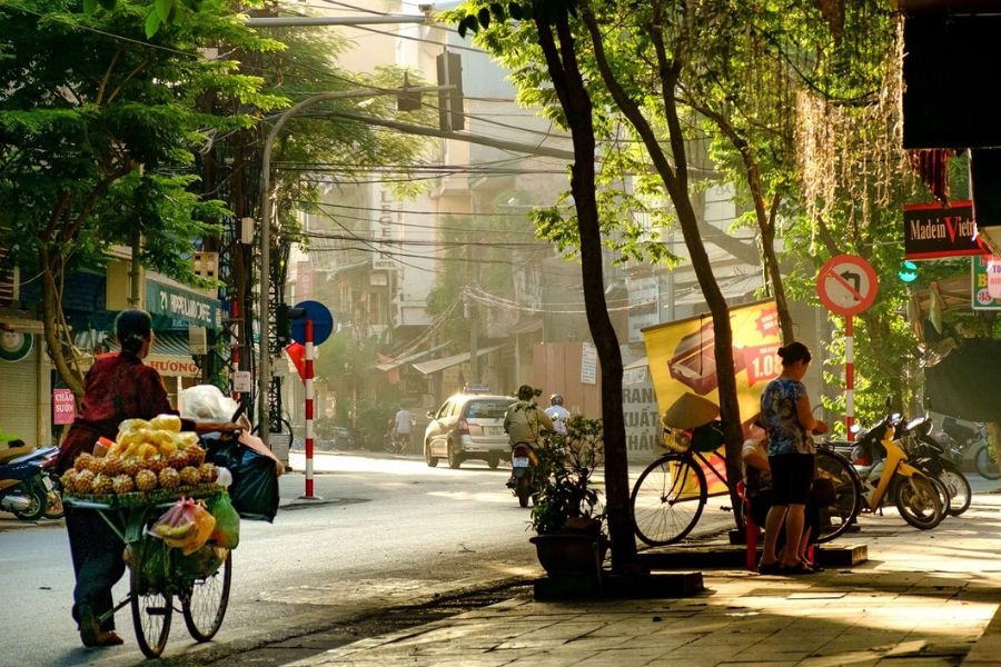 Busy street in Hanoi Old Quarter with traditional shopfronts, pedestrians and motorbikes